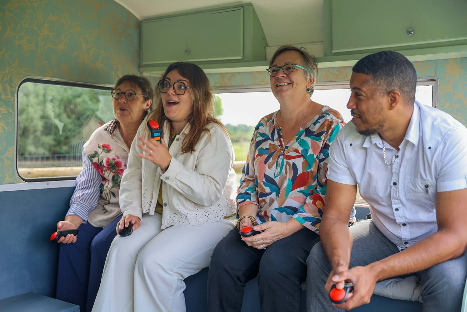 Quatre invités rient en jouant au quiz et au blind test à l’intérieur de la caravane Suzanne, buzzers en main